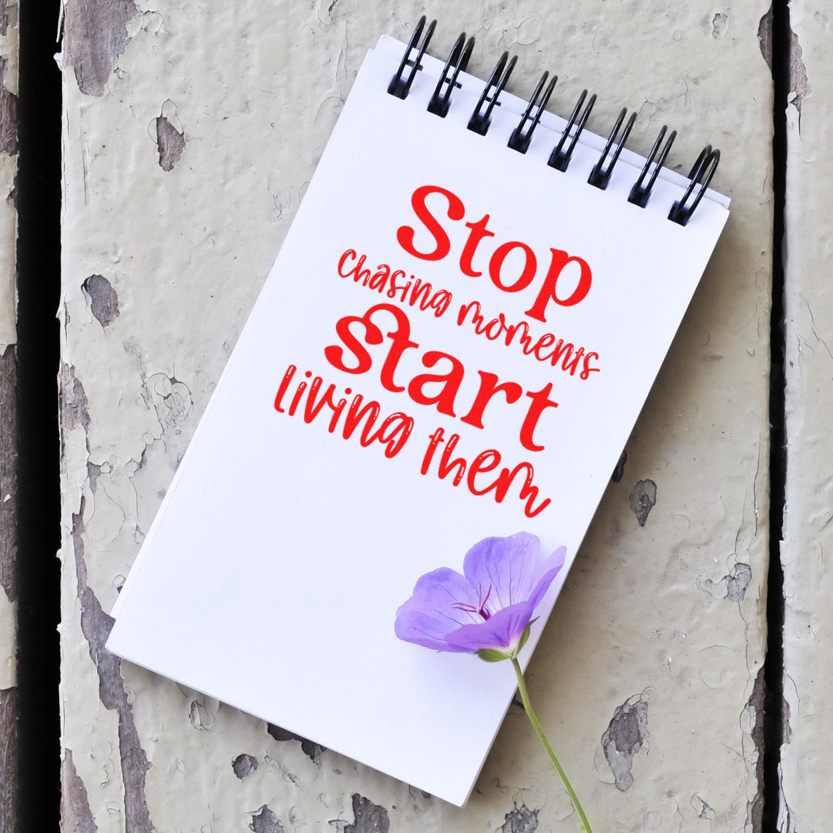 Inspirational rubber stamp with quote, Stop chasing moments, start living them, on a notebook with purple flower.
