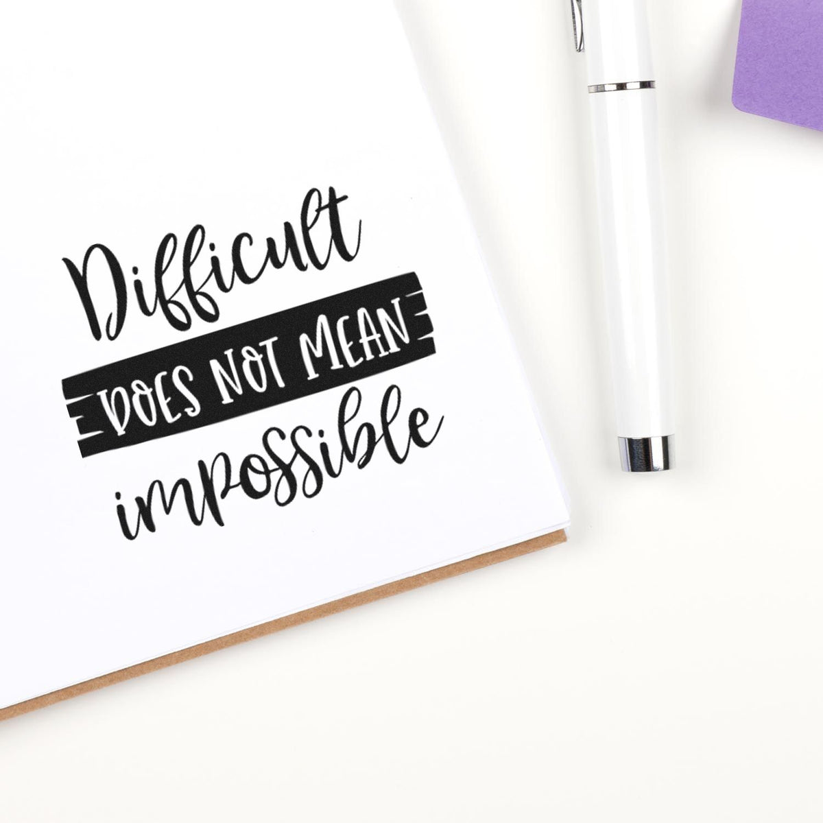 Inspirational rubber stamp quote, Difficult does not mean impossible, stamped on white paper with pen.