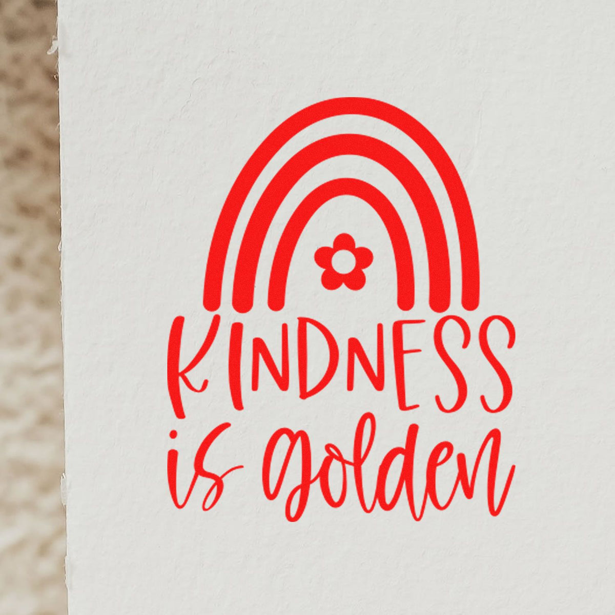 Custom rubber stamp design with rainbow and flower, reading Kindness is Golden in red ink on white paper.
