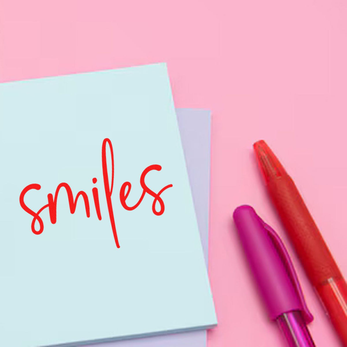 Red smiles rubber stamp design on a pastel sticky note with pens for cheerful stationery projects.