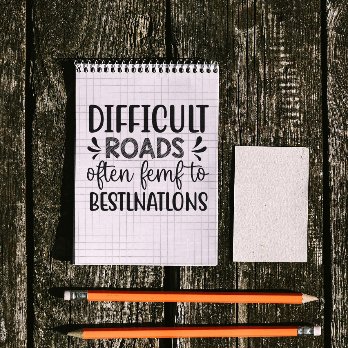 Rubber stamp quote design with inspirational text, Difficult roads often lead to destinations, on a notebook beside a blank stamp block.