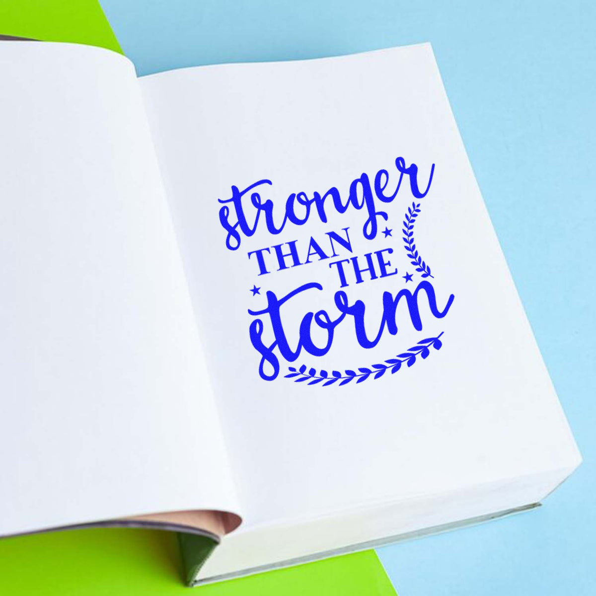 Custom rubber stamp design reading Stronger Than the Storm in blue on an open notebook page.