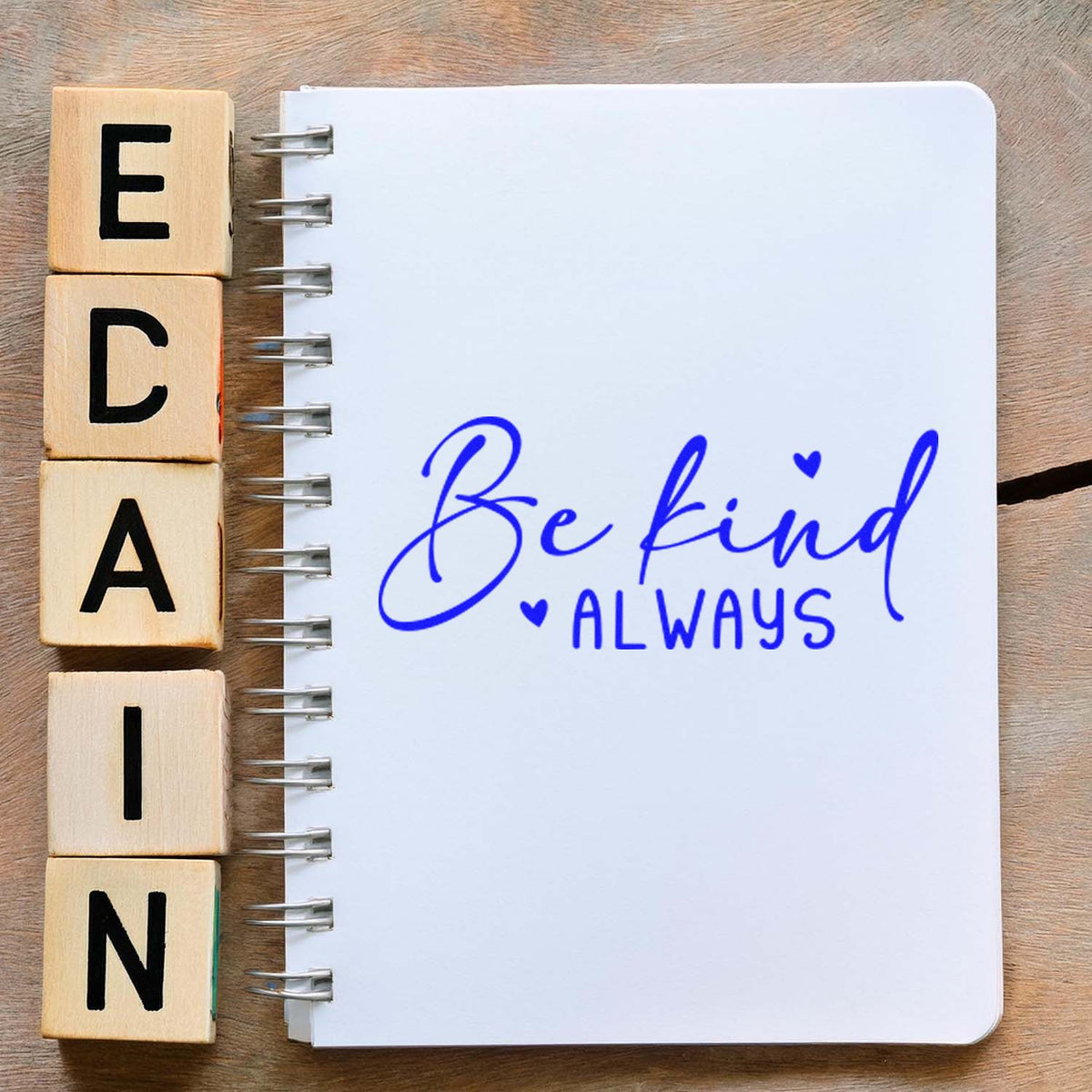 Wooden letter rubber stamp blocks beside a notebook stamped with Be Kind Always in blue ink.