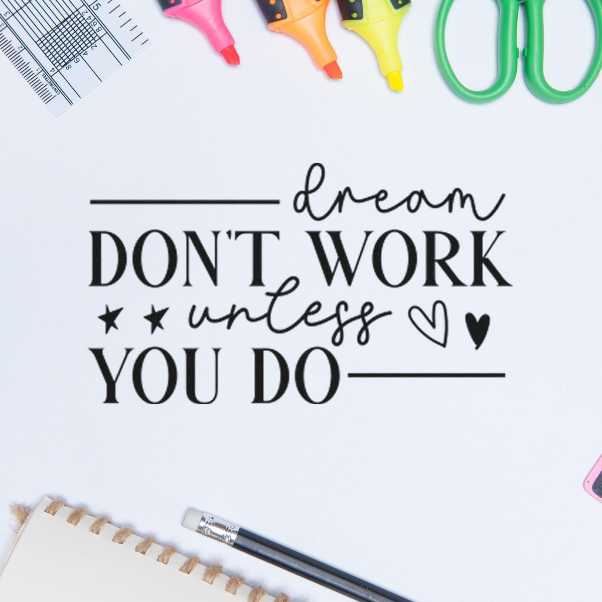 Inspirational rubber stamp quote, "Dream don't work unless you do," on a craft desk with colorful markers and scissors.