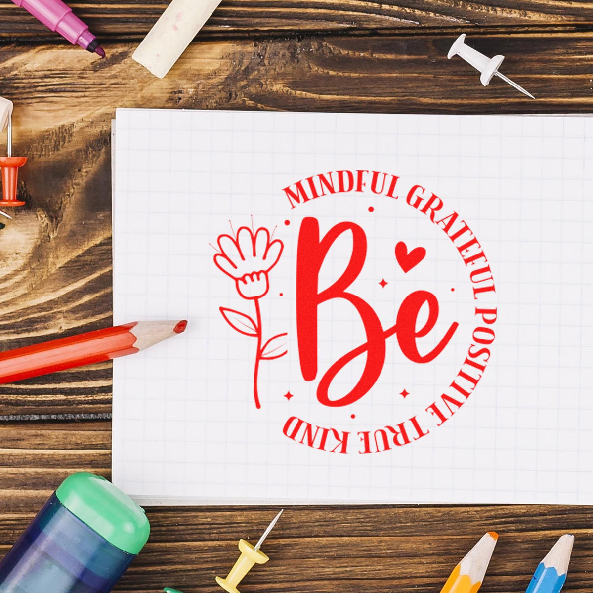 Red mindfulness rubber stamp design reading Be Mindful Grateful Positive True Kind with floral heart on grid paper.