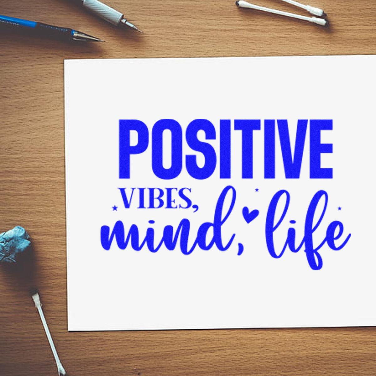 Positive vibes, mind, life custom rubber stamp design displayed on paper with craft tools on a wooden desk.