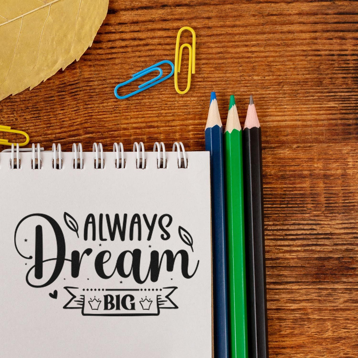 Dream Big rubber stamp impression on spiral notebook with pencils and paper clips, ideal for motivational stationery projects.