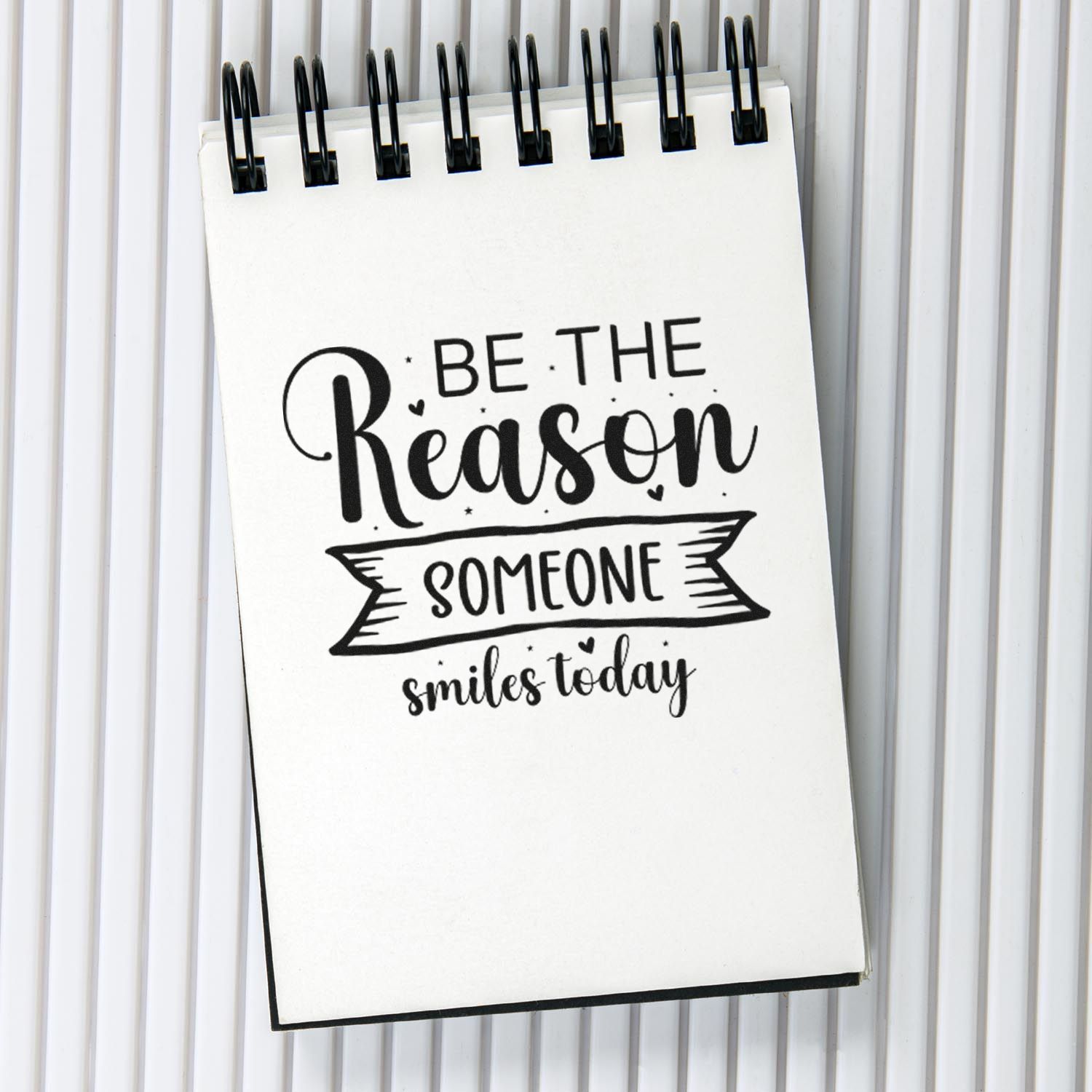 Inspirational rubber stamp impression on a spiral notebook reading Be the reason someone smiles today.