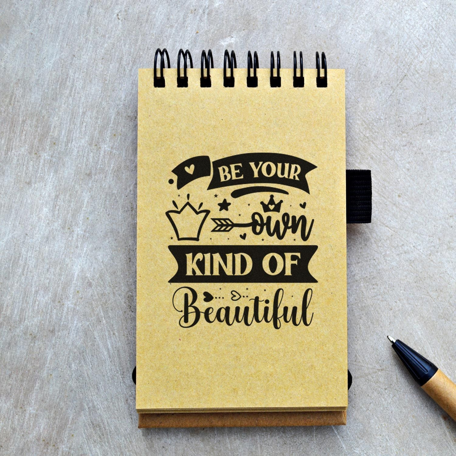 Inspirational custom rubber stamp design reading Be Your Own Kind of Beautiful on a spiral notebook for stationery and crafts.