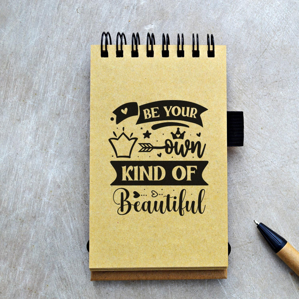 Motivational rubber stamp design on notebook reading Be Your Own Kind of Beautiful with crown and heart accents.