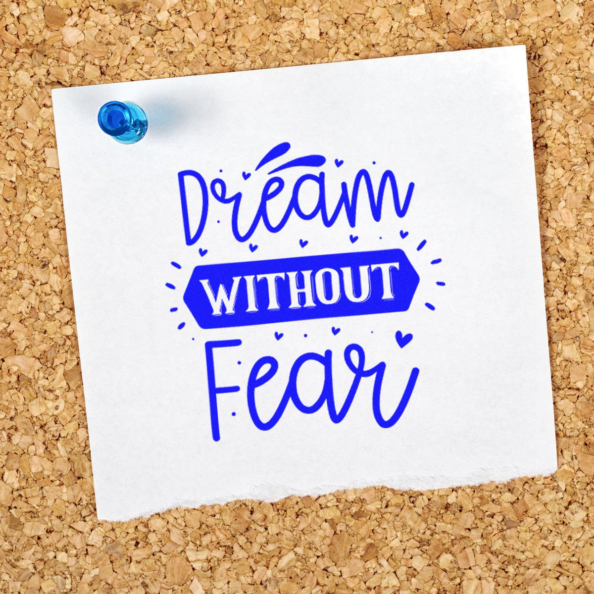 Blue inspirational rubber stamp reading Dream Without Fear pinned to corkboard for DIY crafts and papercrafting.