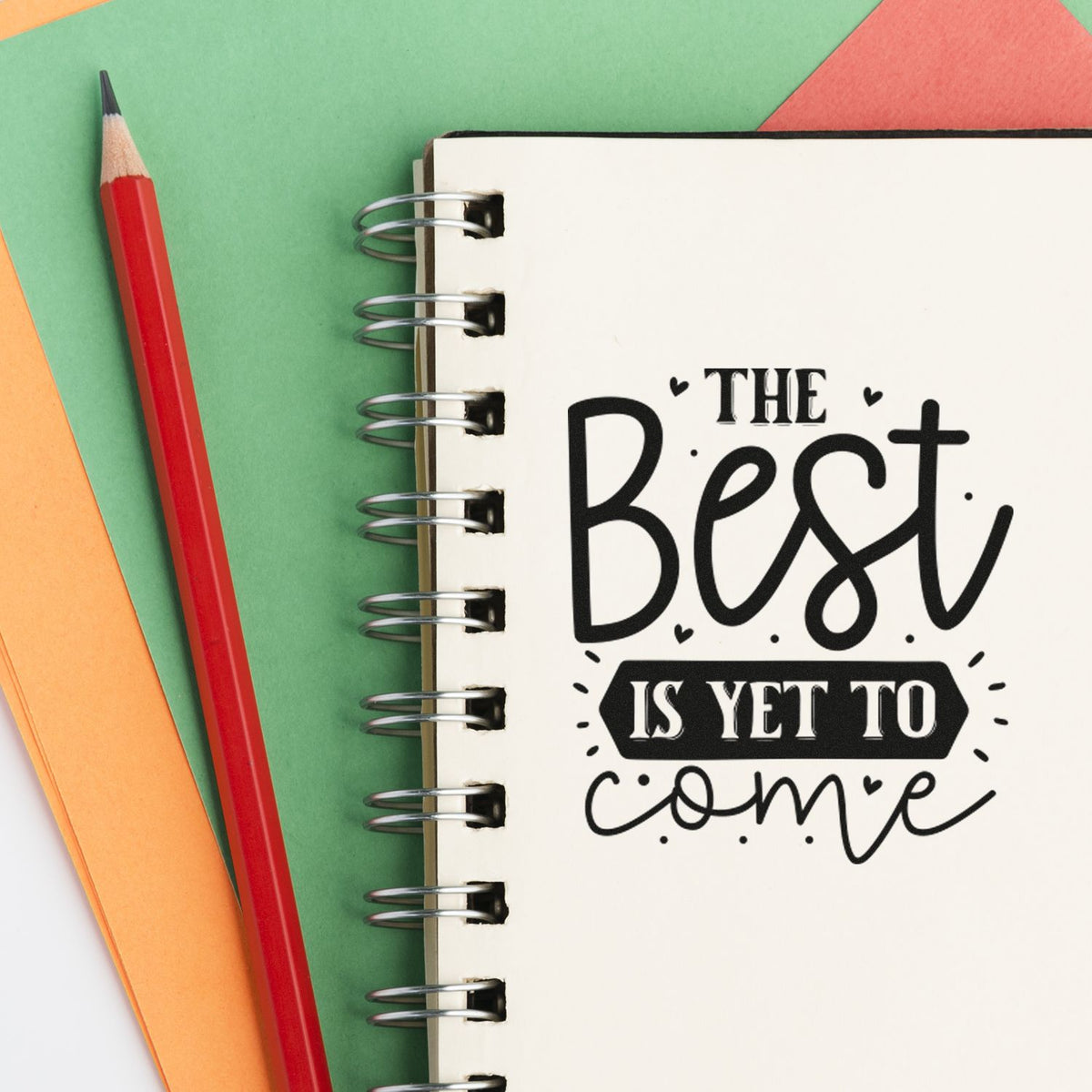 Inspirational rubber stamp design reading The Best Is Yet to Come on a spiral notebook with stationery.