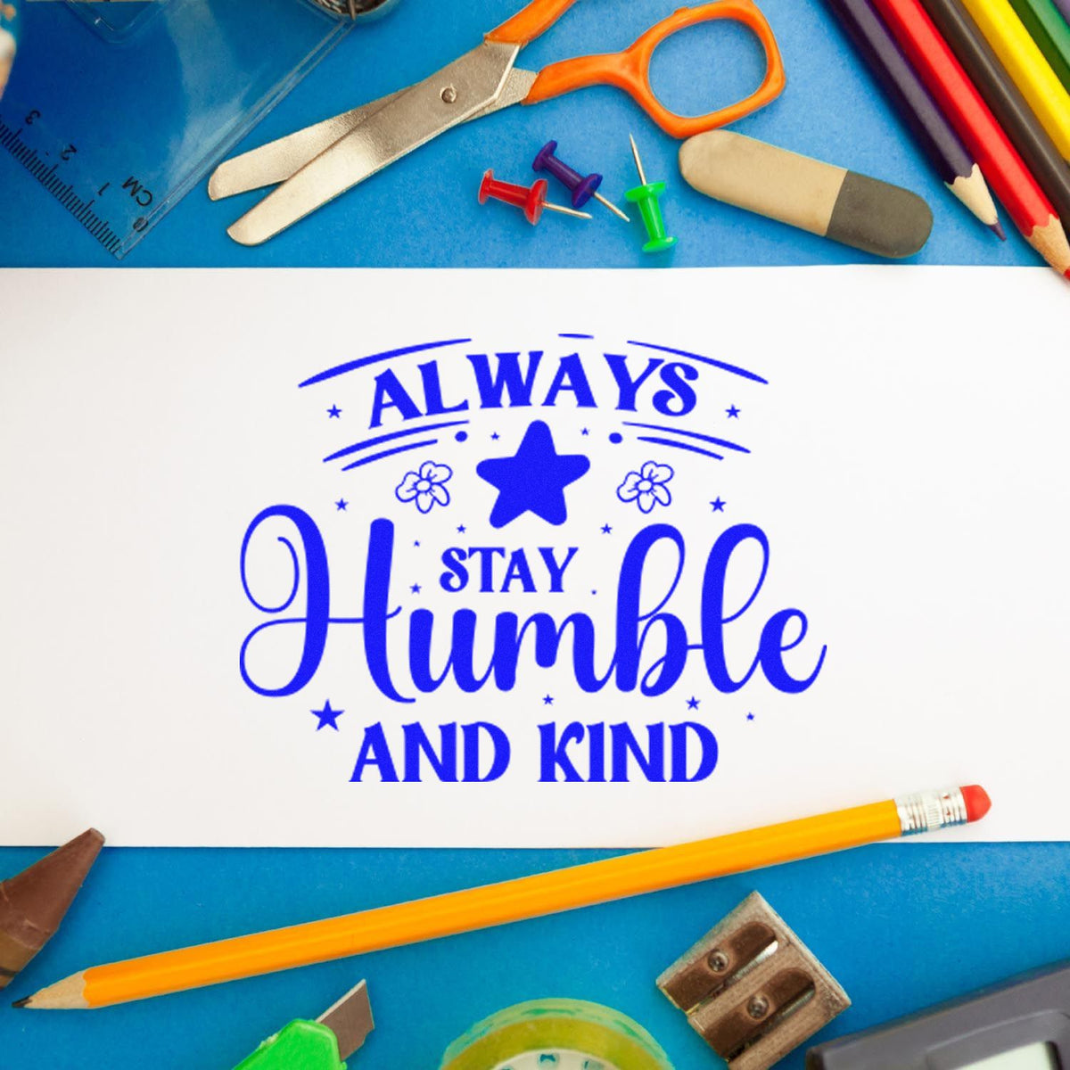 Custom rubber stamp with Always Stay Humble and Kind text, shown with stationery and craft supplies.