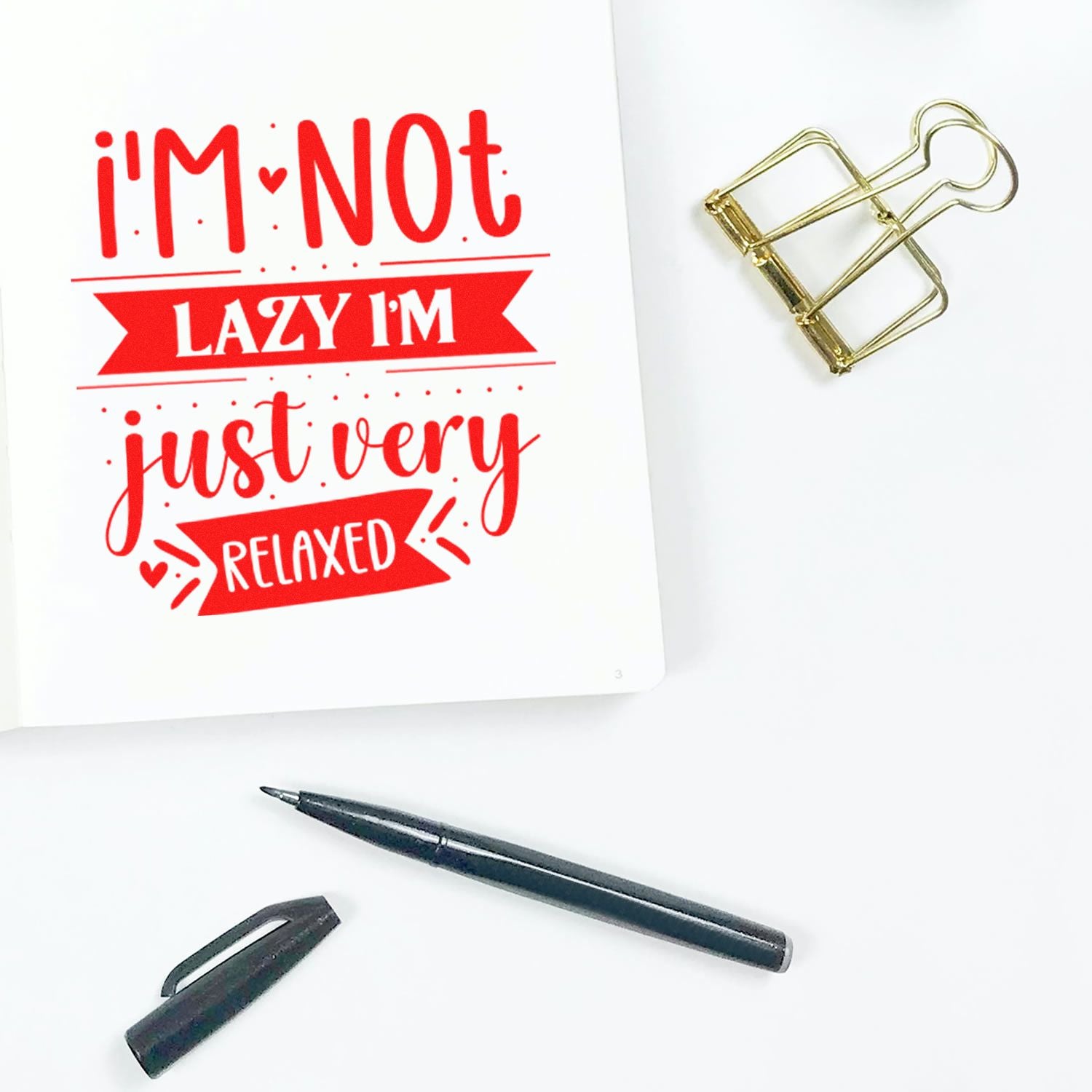 Custom red rubber stamp design reading Im not lazy, Im just very relaxed on notebook page with paperclip and pen.