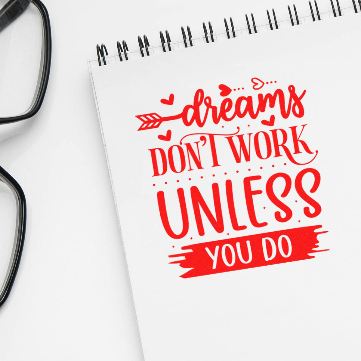 Motivational rubber stamp style quote, Dreams dont work unless you do, in red on a notebook.