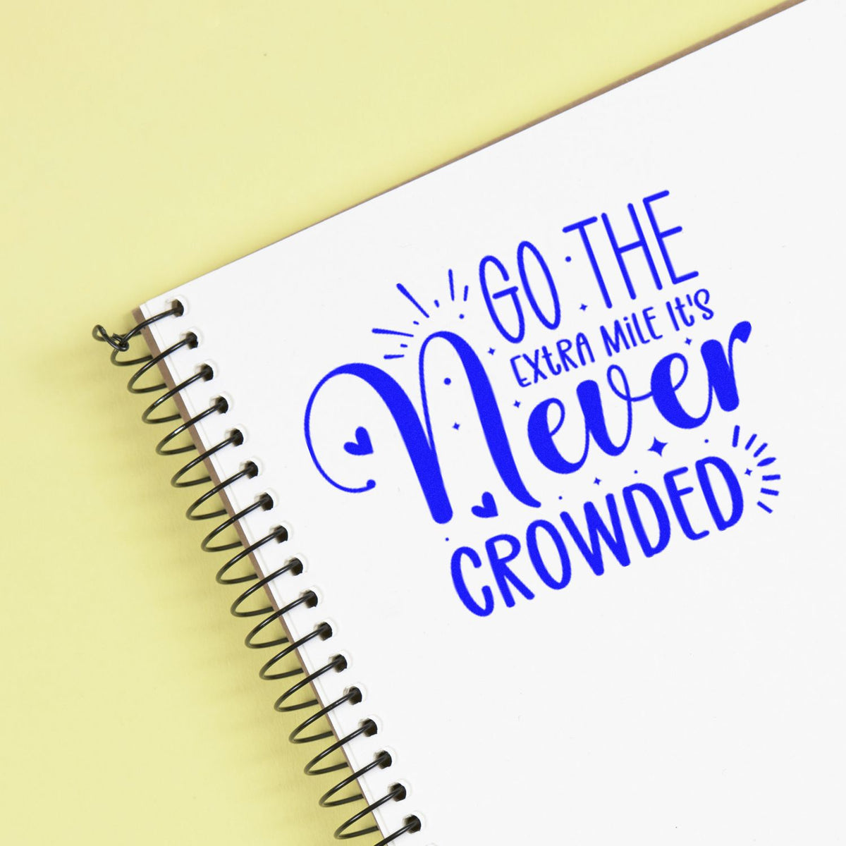 Inspirational rubber stamp on spiral notebook with blue Go the Extra Mile, Its Never Crowded quote.