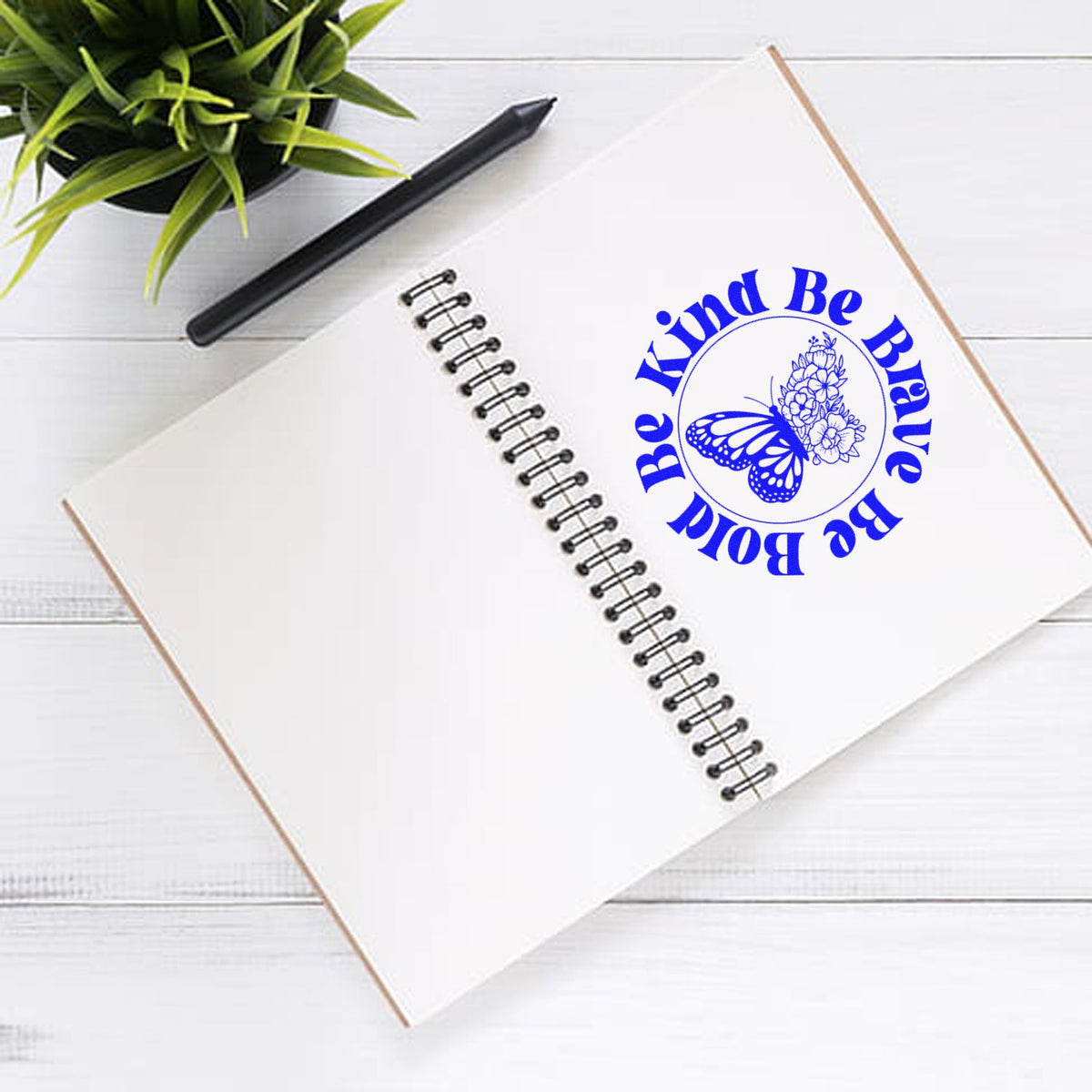 Custom rubber stamp imprint with Be Kind Be Brave Be Bold butterfly floral design on a spiral notebook.