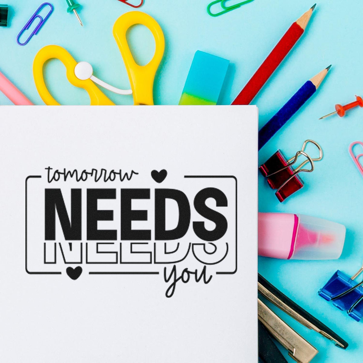 Inspirational rubber stamp reading Tomorrow needs you on paper, surrounded by colorful stationery and office supplies.