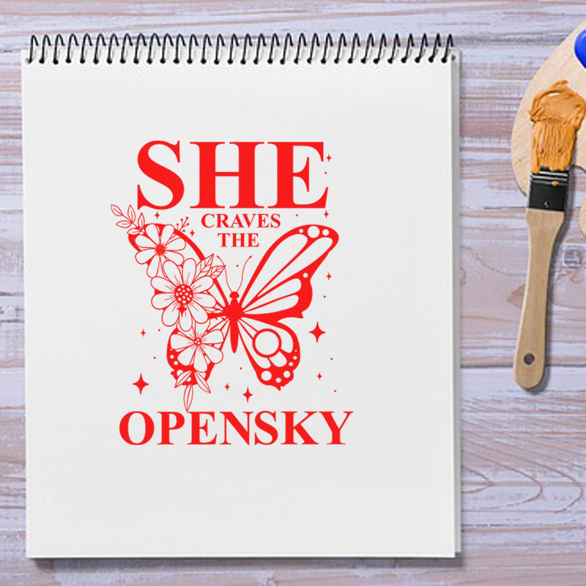 Butterfly floral rubber stamp design reading She Craves the Open Sky on a notebook page.