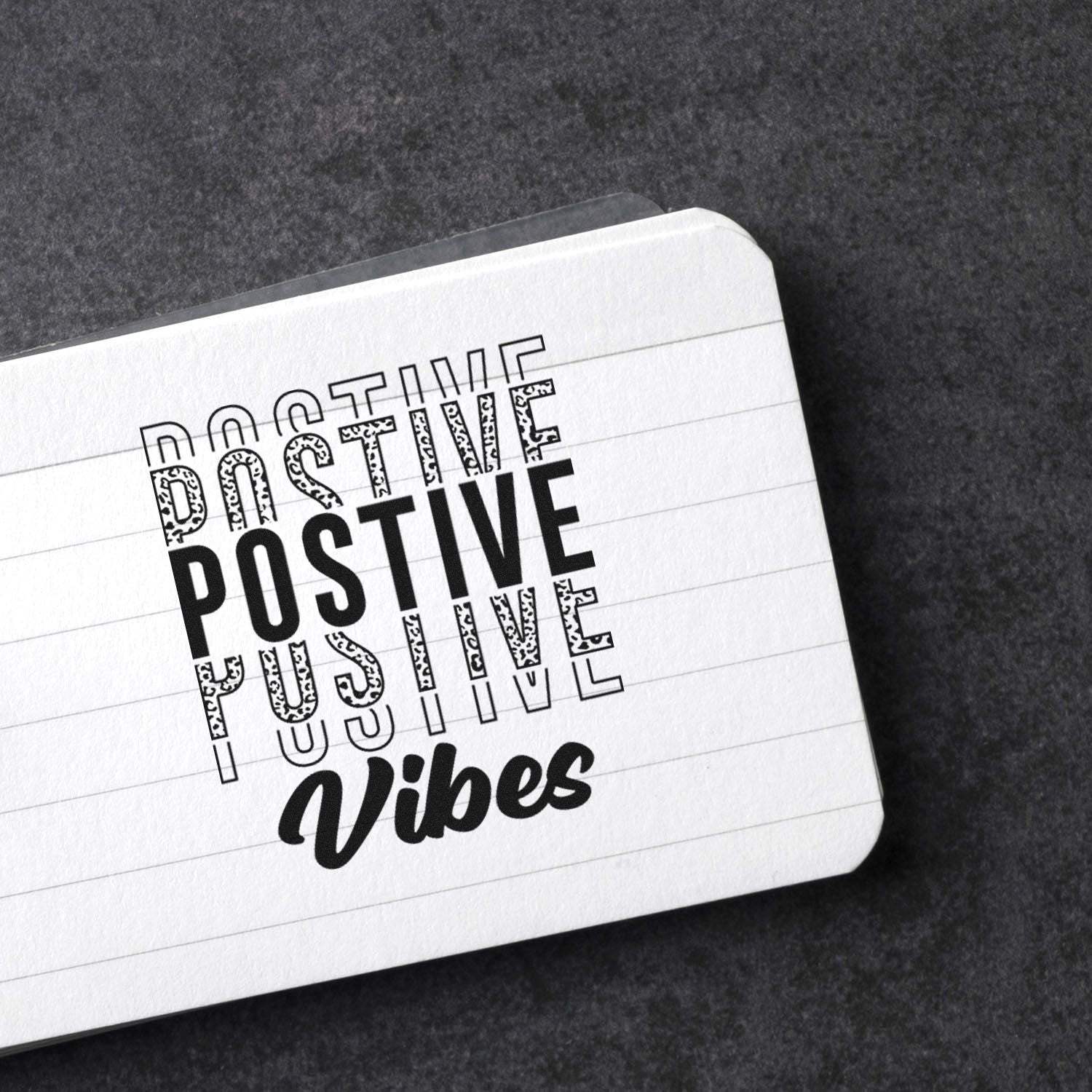 Positive Vibes rubber stamp design on lined paper, featuring bold black typography for motivational stationery.
