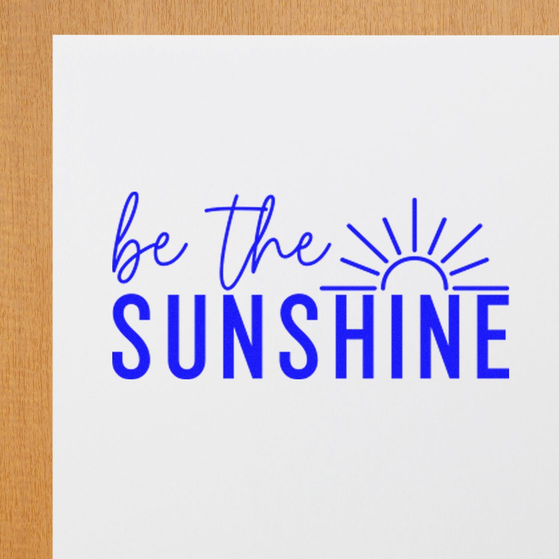 Motivational rubber stamp design with blue Be the Sunshine text and sun icon on white paper.