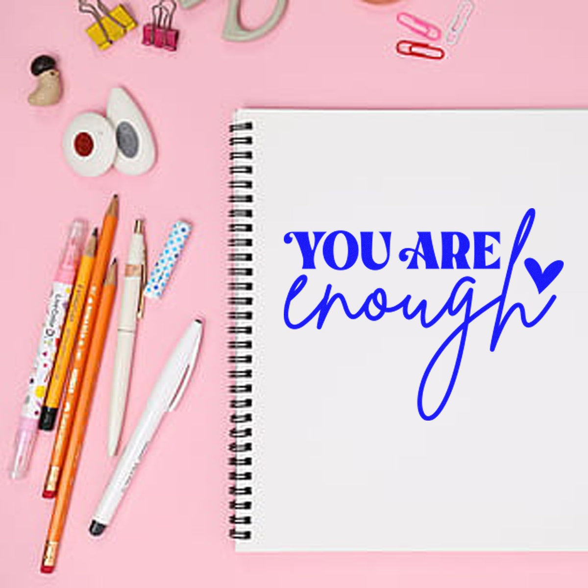 You Are Enough motivational rubber stamp for notebooks, with blue lettering on a planner and pink stationery background.