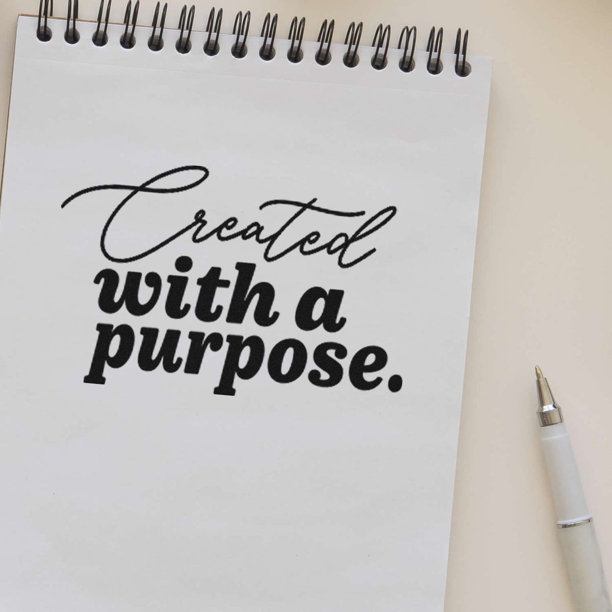 Custom rubber stamp reading Created with a purpose displayed on a notebook page with a pen.