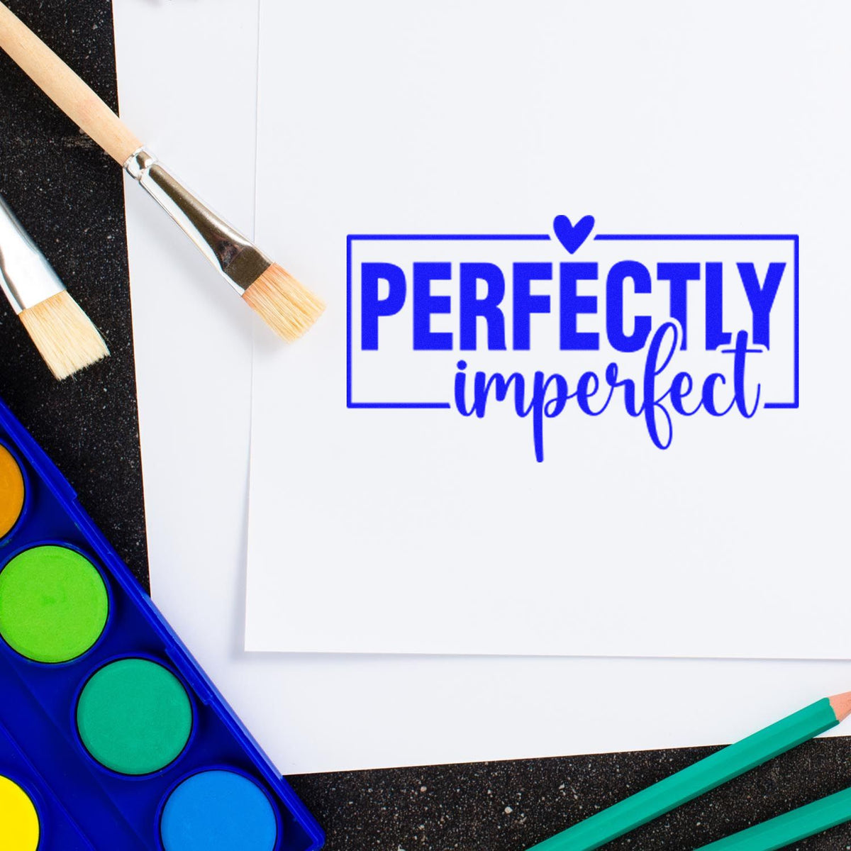 Perfectly imperfect rubber stamp on paper with paintbrushes and watercolor palette for handmade craft projects.
