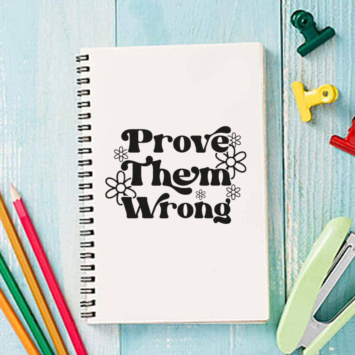 Inspirational rubber stamp design with Prove Them Wrong on a notebook, surrounded by colorful stationery.