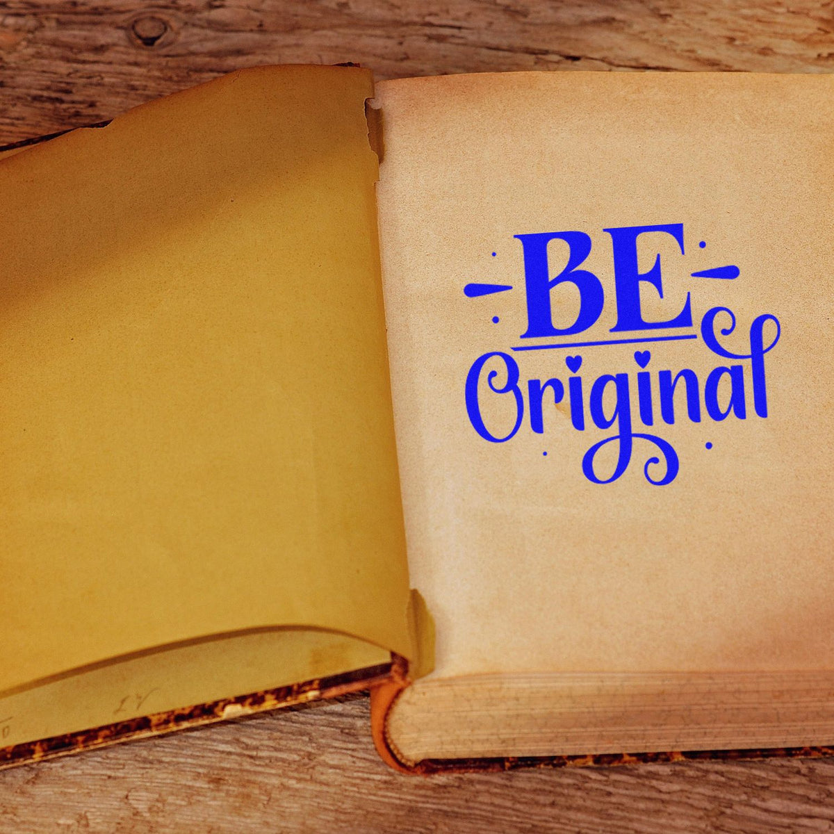 Blue "Be Original" rubber stamp impression on an open vintage book page for custom motivational crafting.