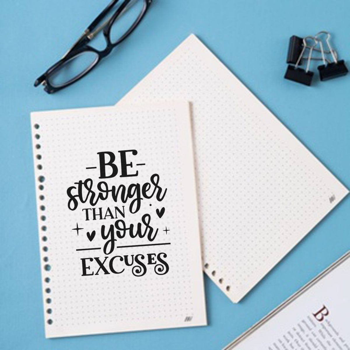 Motivational rubber stamp design reading Be stronger than your excuses on dotted notebook pages with office supplies.
