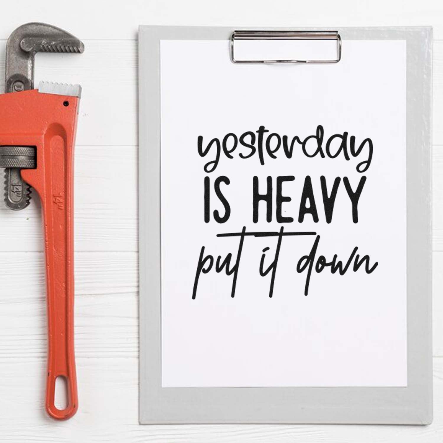 Motivational rubber stamp quote, Yesterday is heavy, put it down, on a clipboard beside a pipe wrench for trades.