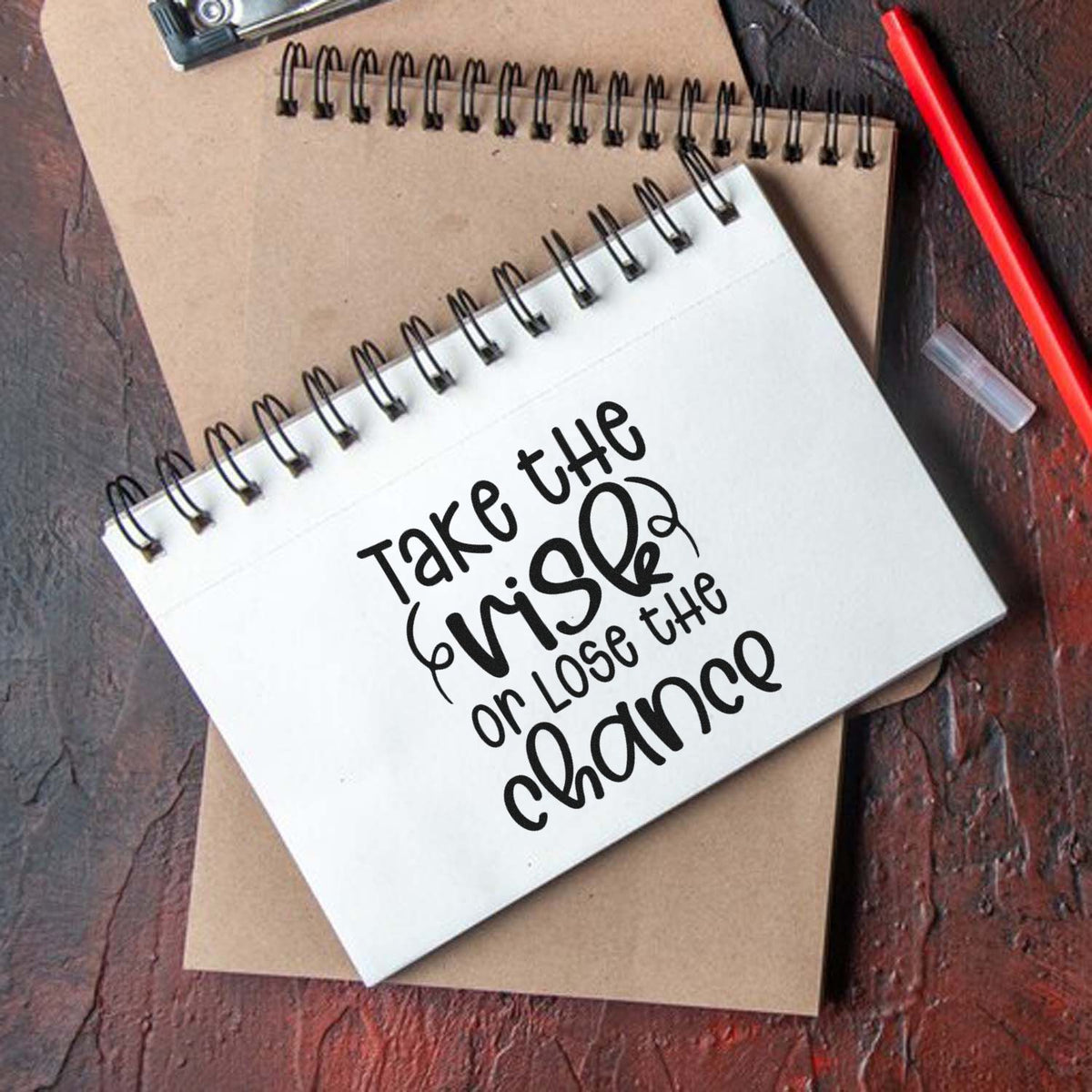Inspirational rubber stamp design with Take the risk or lose the chance on a spiral notebook for crafting and journaling.