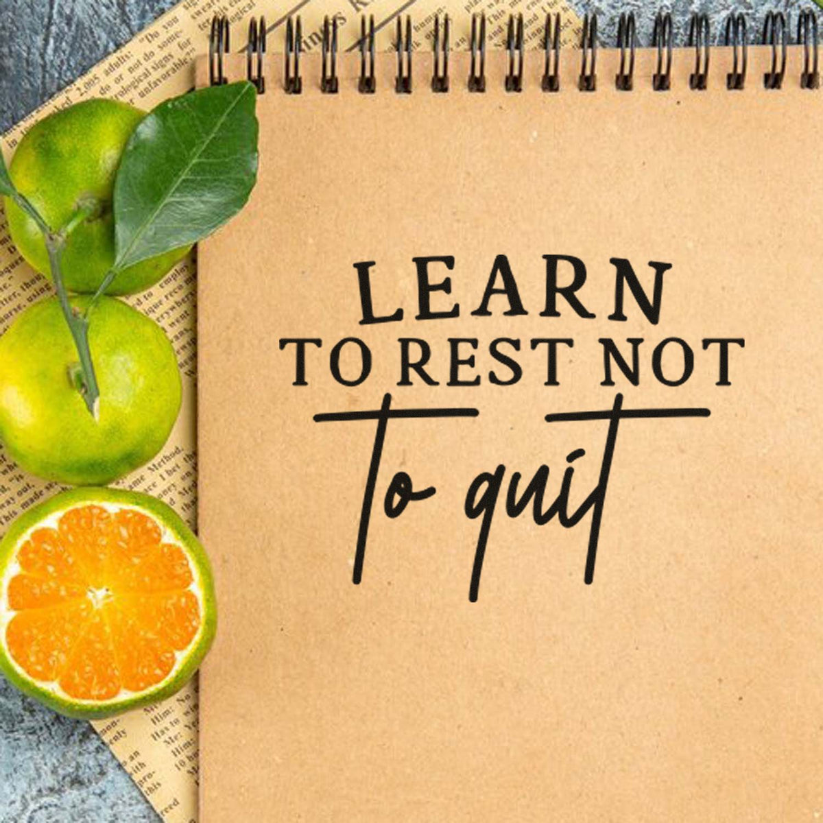 Inspirational custom rubber stamp quote, Learn to rest not to quit, on kraft notebook with citrus and leaves.