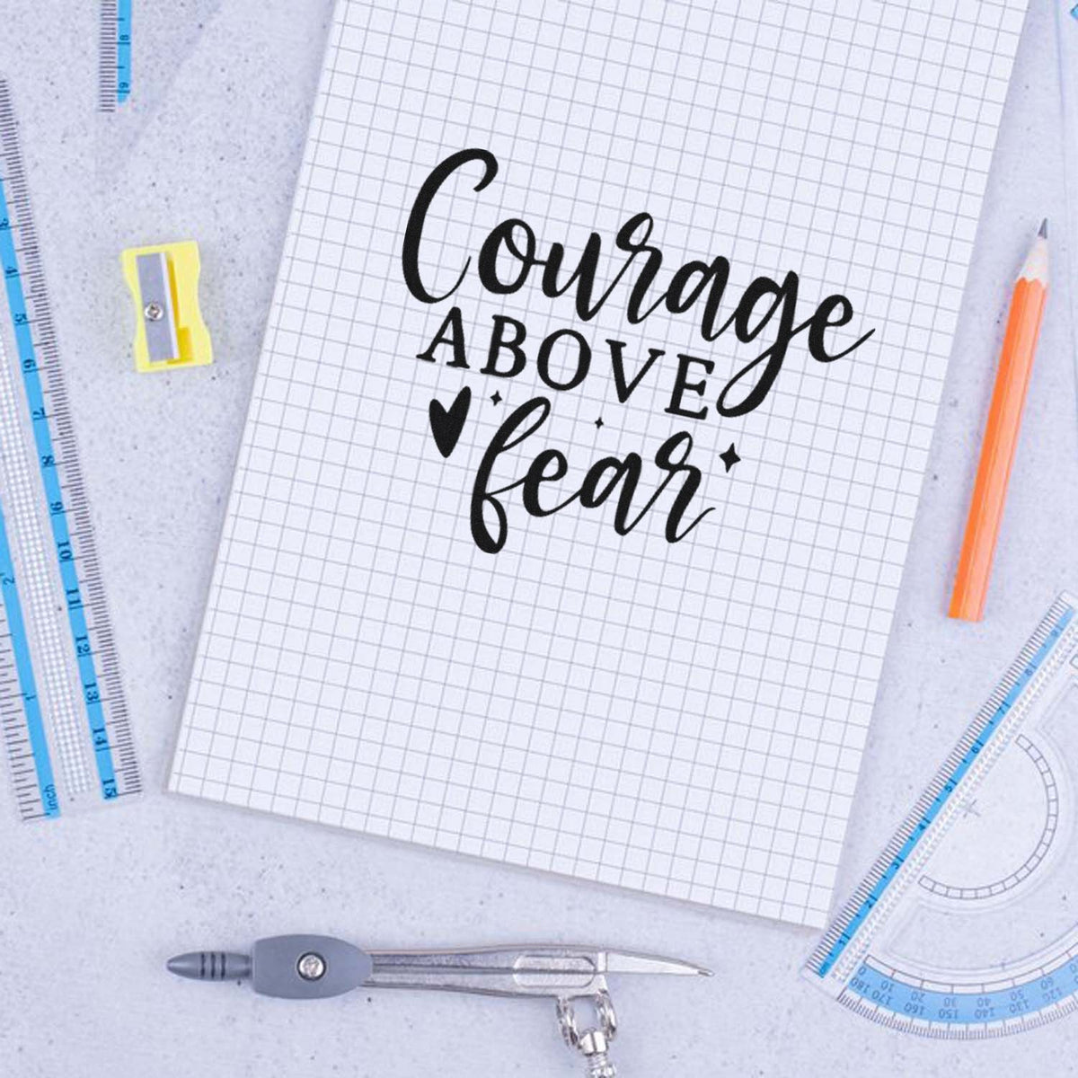 Rubber stamp design with quote Courage above fear in black script and bold type on graph paper with school supplies.