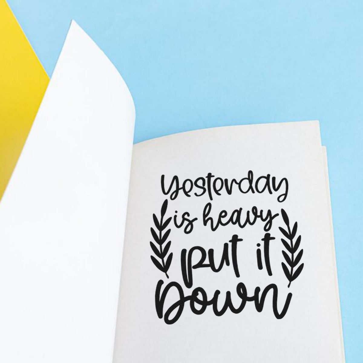 Inspirational rubber stamp design with the quote Yesterday is heavy, put it down and leafy accents on white paper.