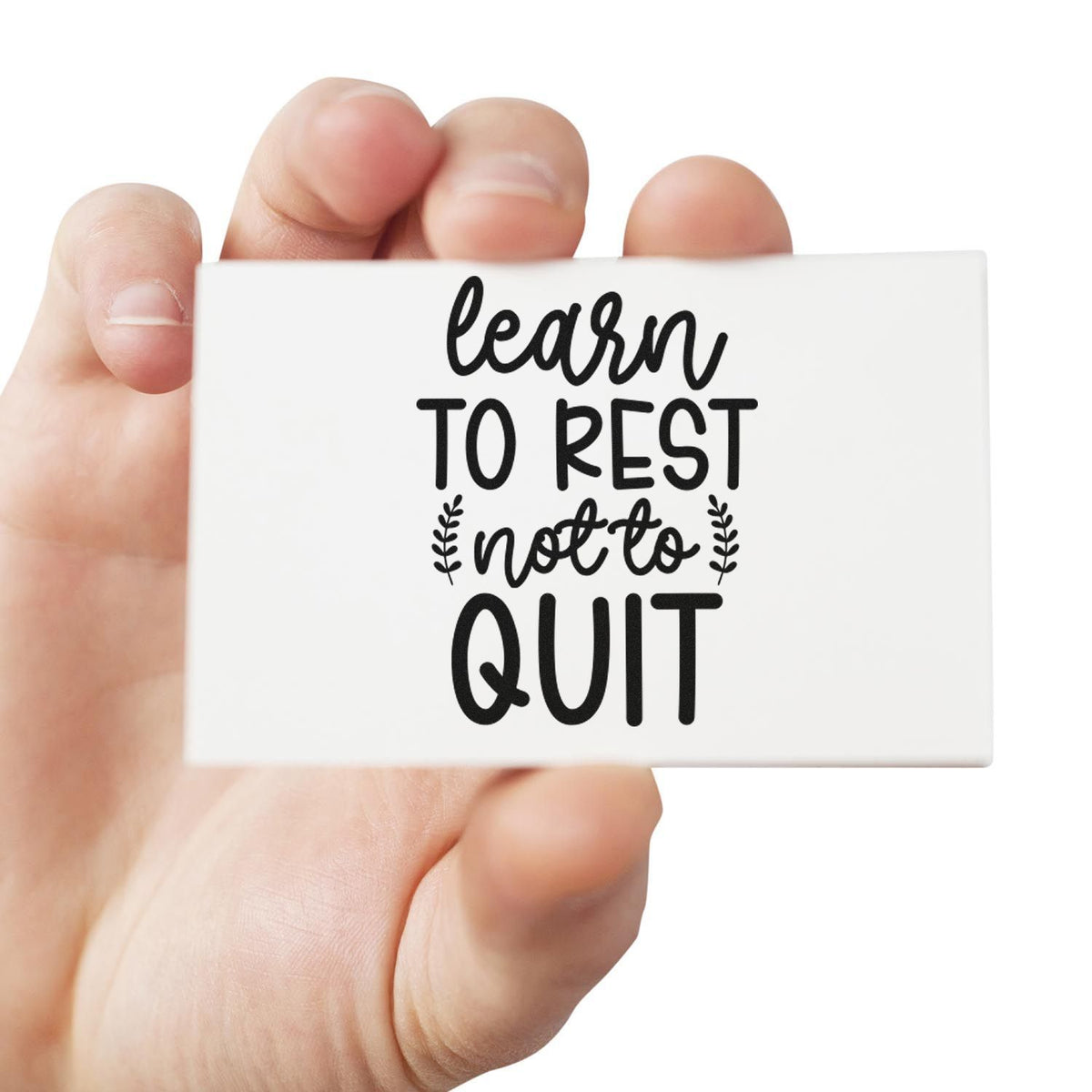Hand holding custom rubber stamp with learn to rest not to quit quote for self-care and motivational crafting.