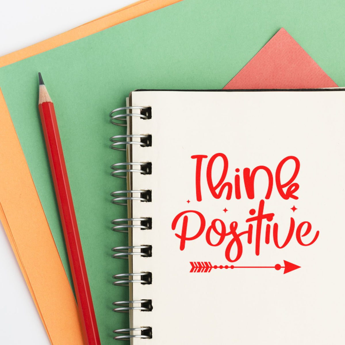 Think Positive rubber stamp design on a notebook, with red pencil and colorful paper background for motivational stationery projects.