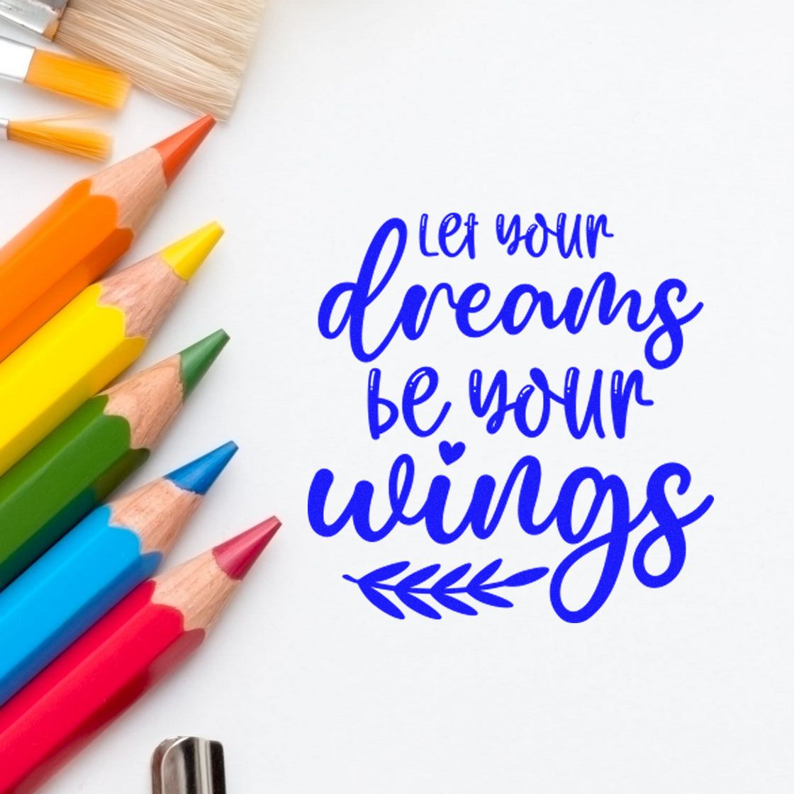 Inspirational rubber stamp quote, Let your dreams be your wings, with colorful pencils on white paper.