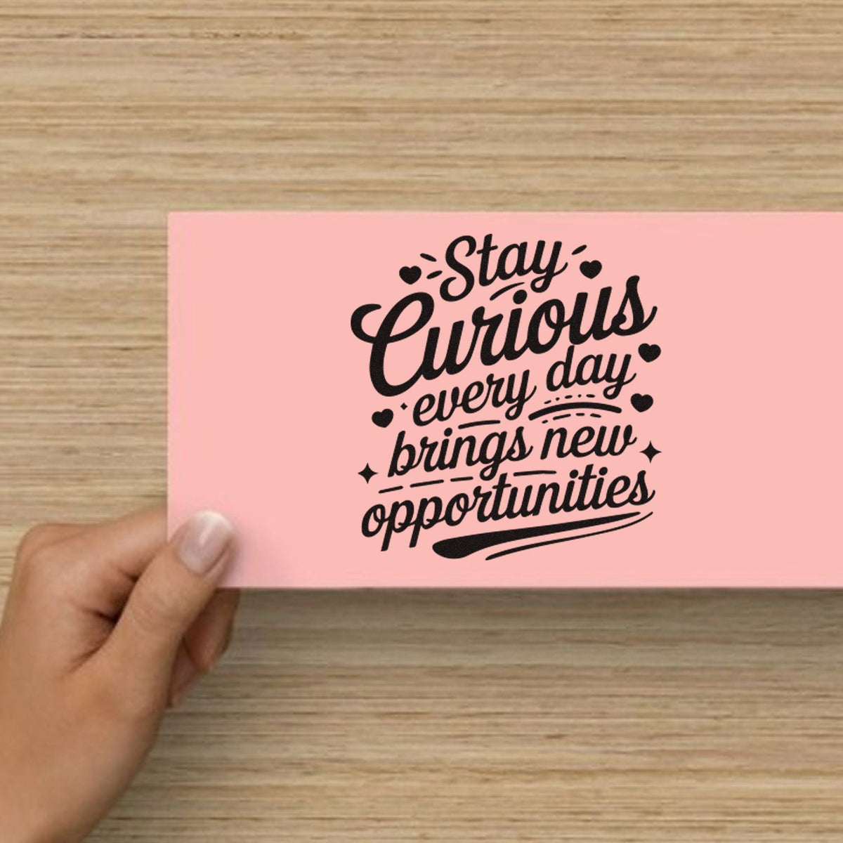 Hand holding a pink card with a motivational rubber stamp quote: Stay Curious, every day brings new opportunities.