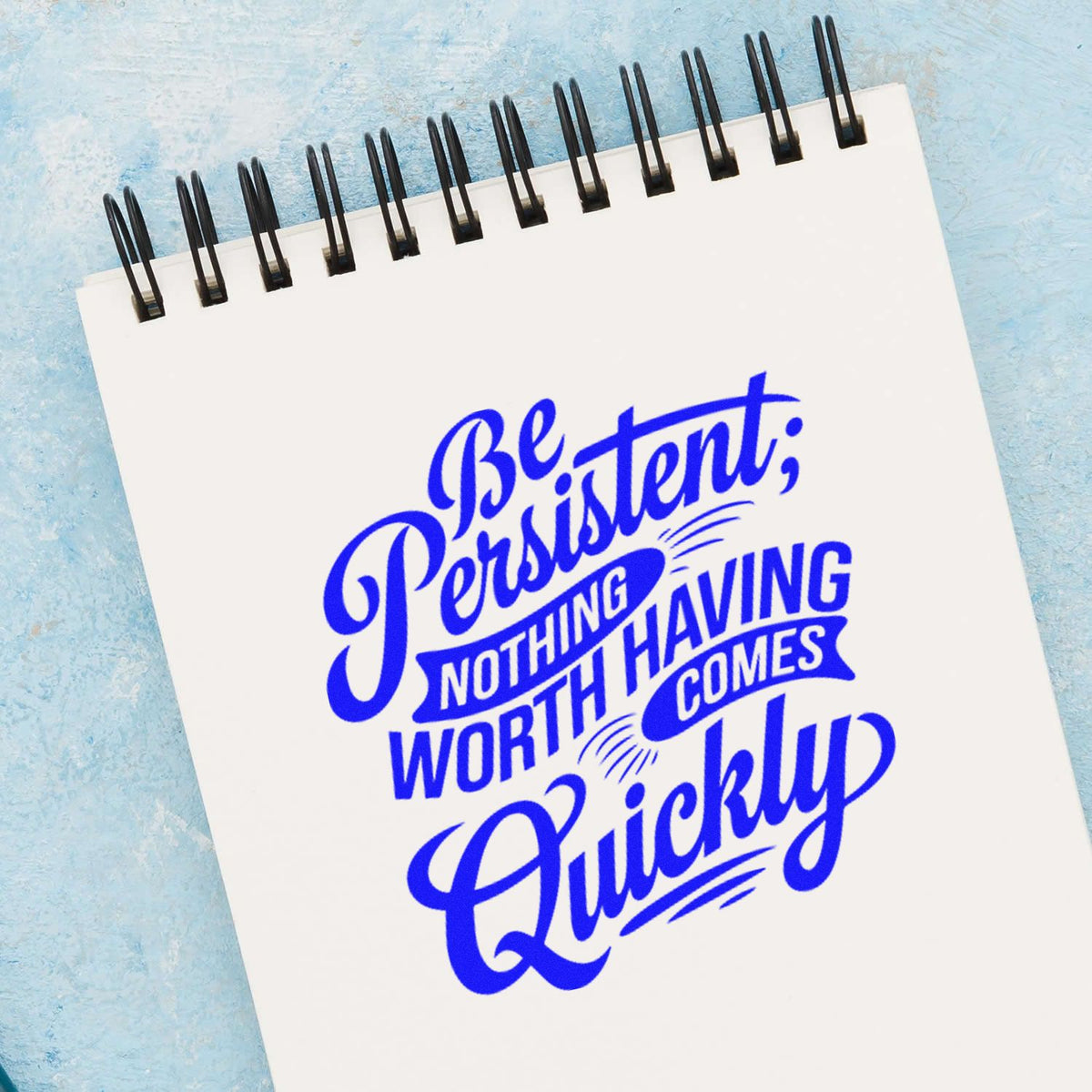 Inspirational custom rubber stamp on notebook: Be persistent; nothing having worth comes quickly in bold blue lettering.