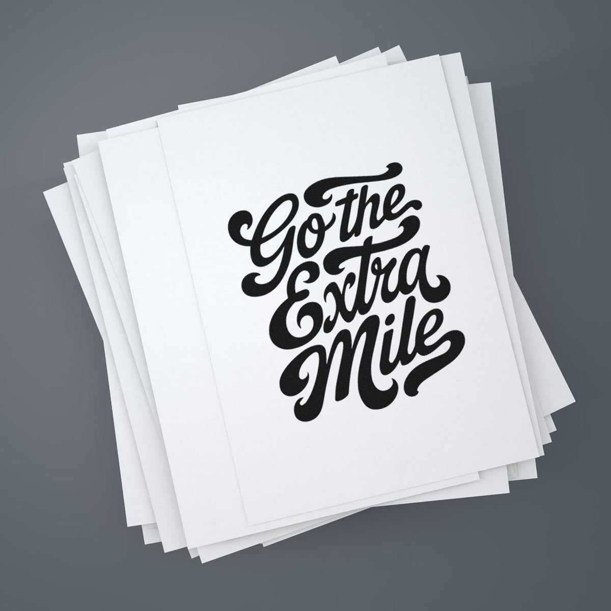 Motivational rubber stamp reading Go the Extra Mile on stacked white paper sheets.