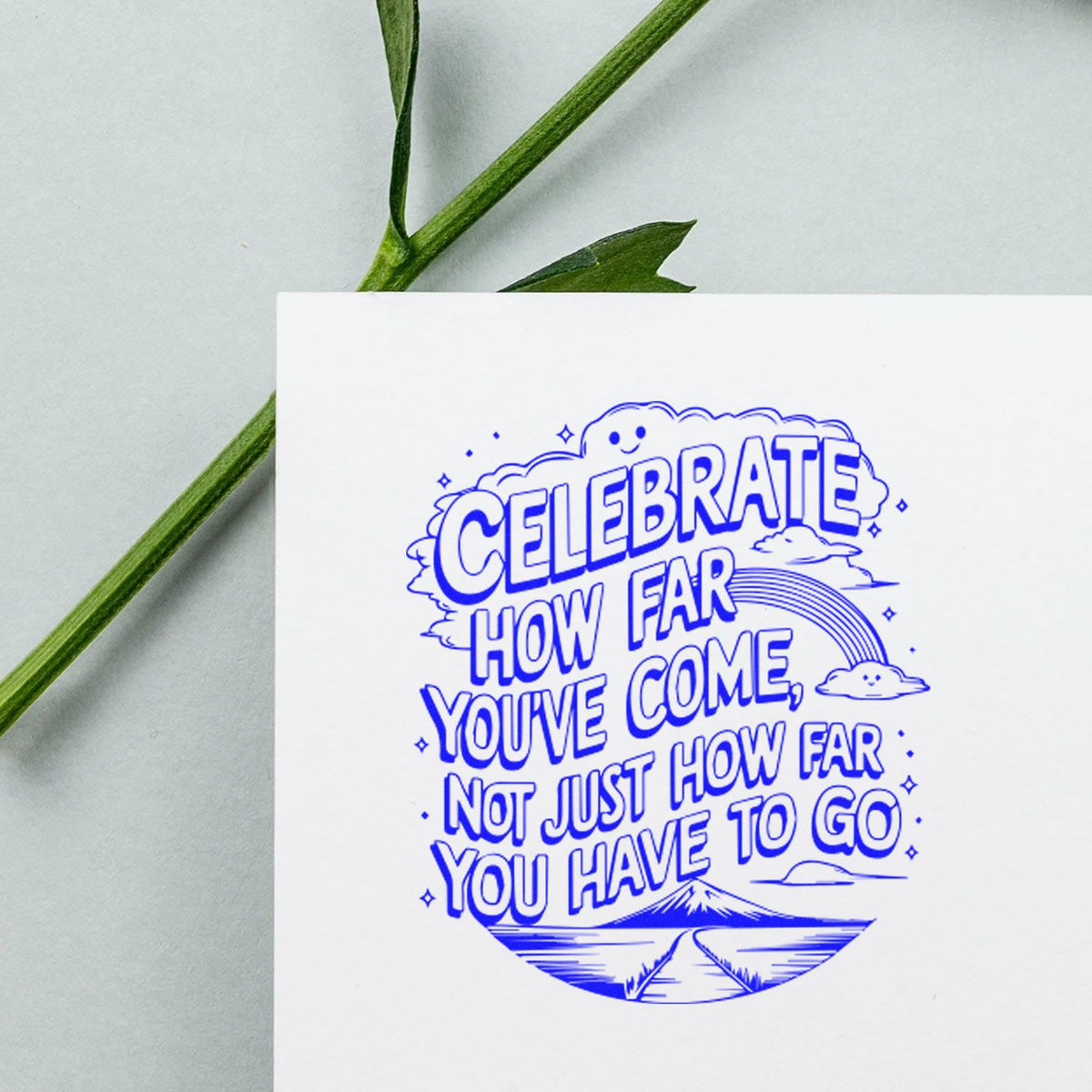 Motivational rubber stamp impression with quote, Celebrate how far youve come, not just how far you have to go, in blue on card.