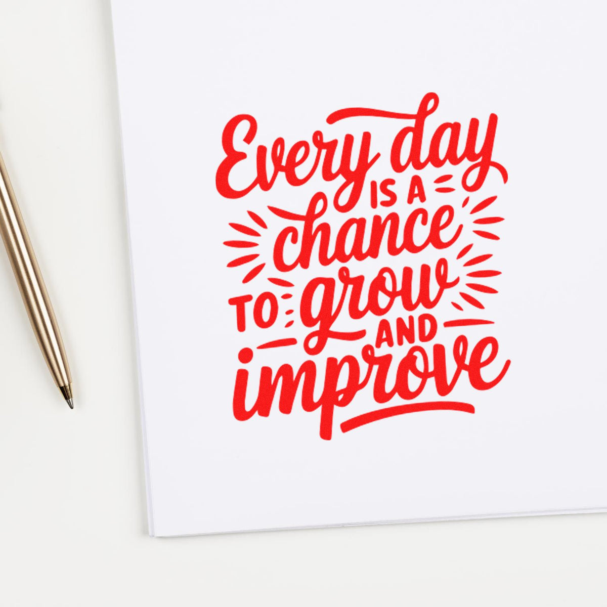 Red motivational rubber stamp on white paper reading Every day is a chance to grow and improve with pen beside it.