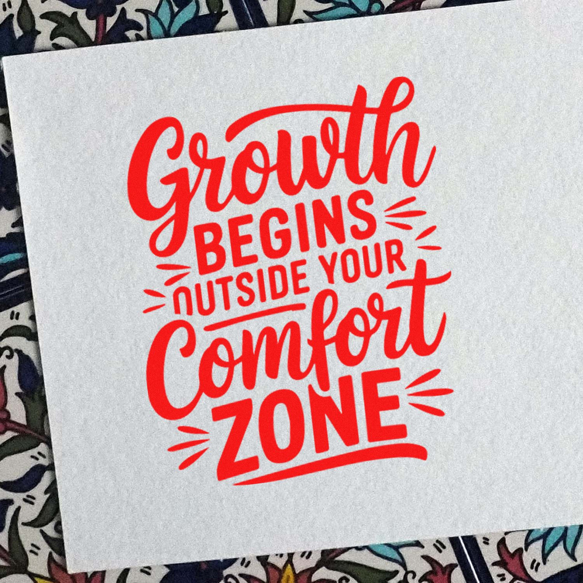 Red motivational rubber stamp imprint reading Growth begins outside your comfort zone on white paper.