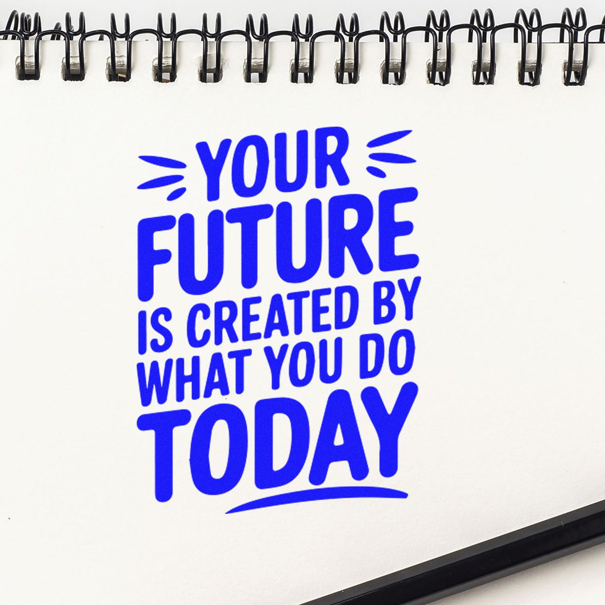 Custom rubber stamp with blue motivational quote, Your future is created by what you do today, on a spiral notebook.