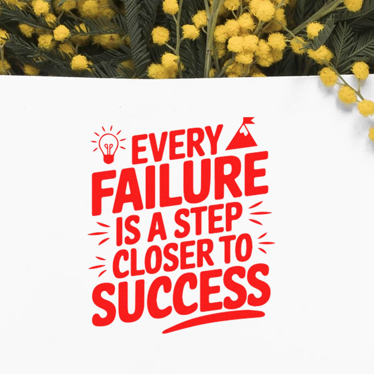 Red inspirational rubber stamp reading Every failure is a step closer to success with lightbulb icon on white paper.
