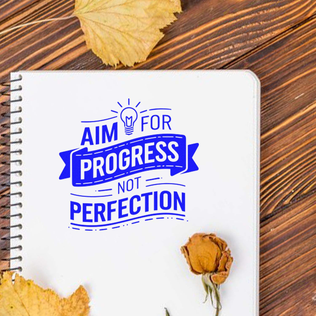Custom motivational rubber stamp reading Aim for Progress Not Perfection on a notebook, ideal for journals and planners.