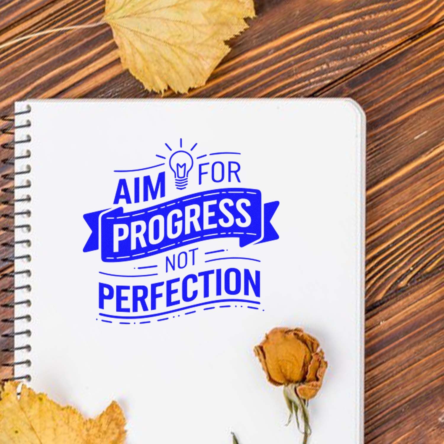 Blue motivational rubber stamp design saying Aim for progress, not perfection on a notebook for planners and journals.