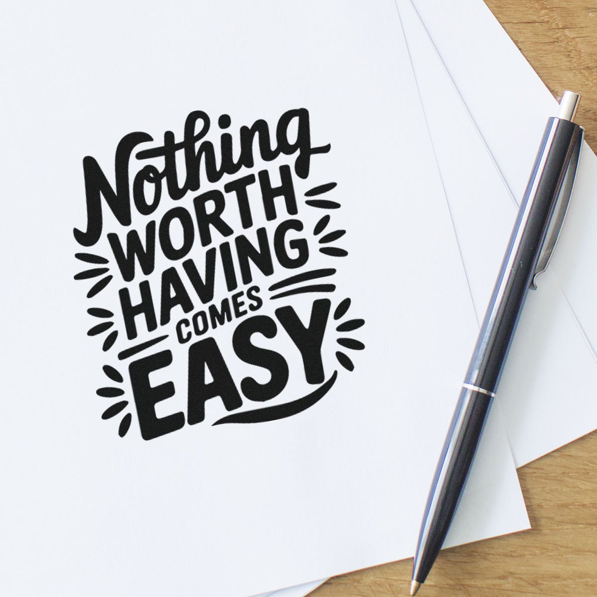 Inspirational rubber stamp design reading Nothing Worth Having Comes Easy stamped on paper beside a pen.